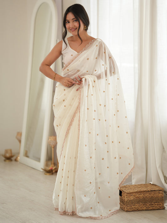 Woman wearing off white satin saree with ornamented surface design and off white blouse