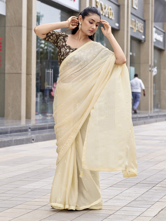 Woman wearing cream satin silk saree with ornamented surface design and brown blouse