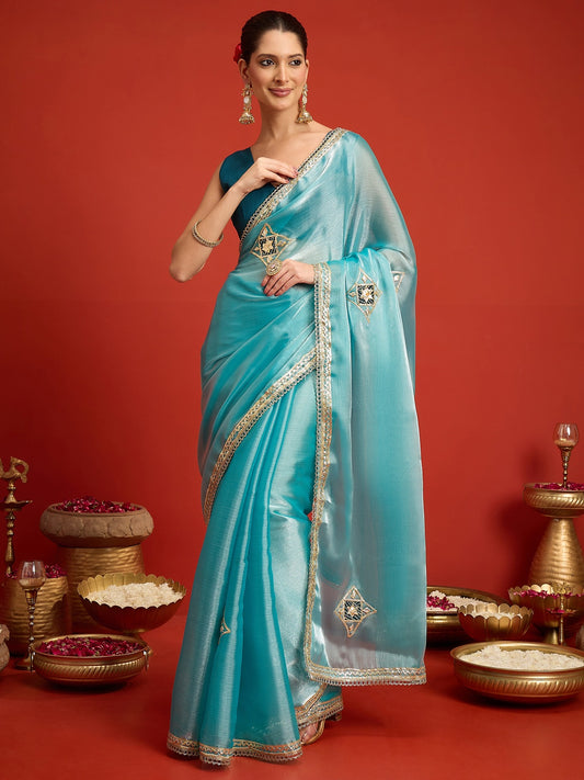 Woman wearing light blue paper silk saree with ornamented surface design and teal blouse