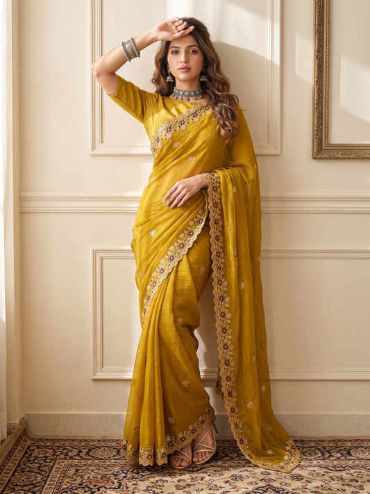 Woman wearing mustard tissue saree with ornamented surface design and mustard blouse