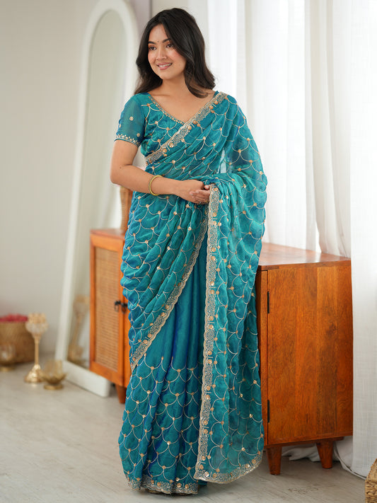 Woman wearing teal blue tissue saree with ornamented surface design and teal blue blouse