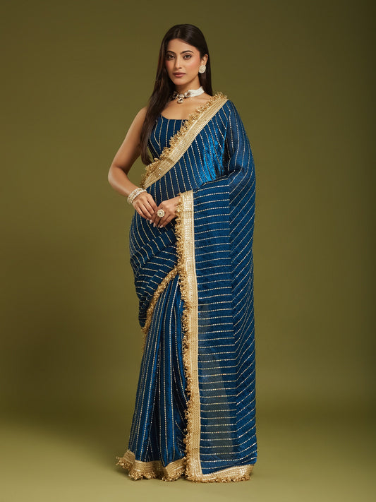 Woman wearing teal blue satin saree with ornamented surface design and teal blue blouse