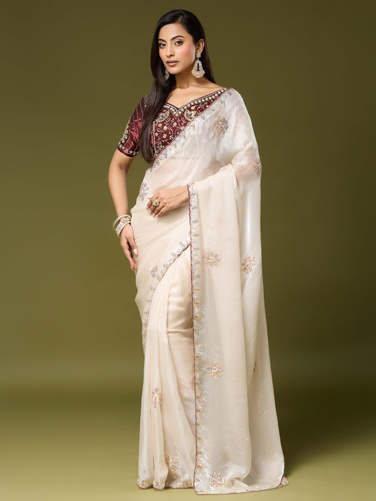 Woman wearing off white satin silk saree with ornamented surface design and maroon blouse