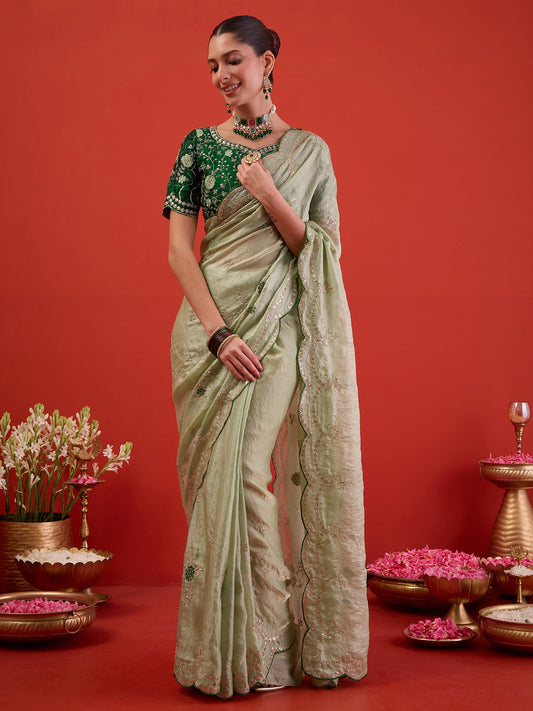 Woman wearing light green satin silk saree with ornamented surface design and dark green blouse