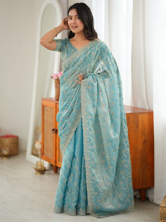 Woman wearing light blue tissue saree with ornamented surface design and light blue blouse