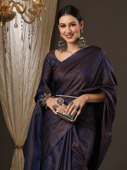 Woman in a dark blue saree holding a clutch against a draped curtain background