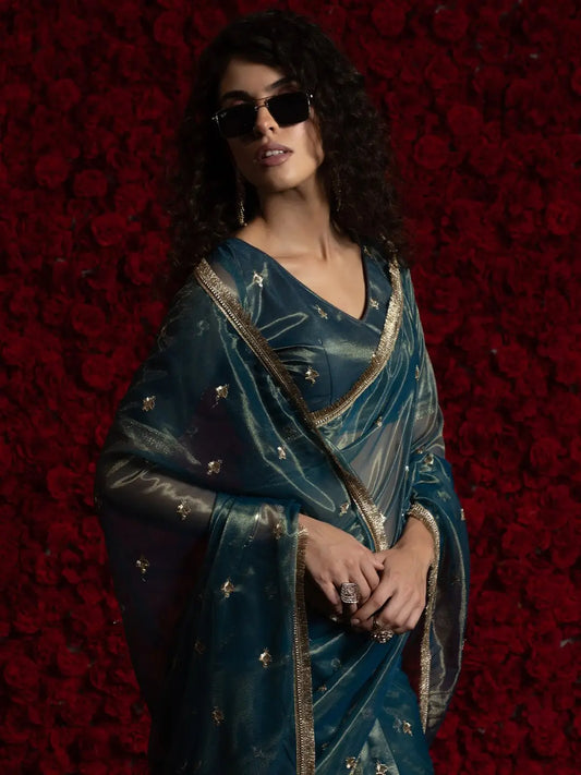 Woman wearing a blue saree with gold details against a red floral background