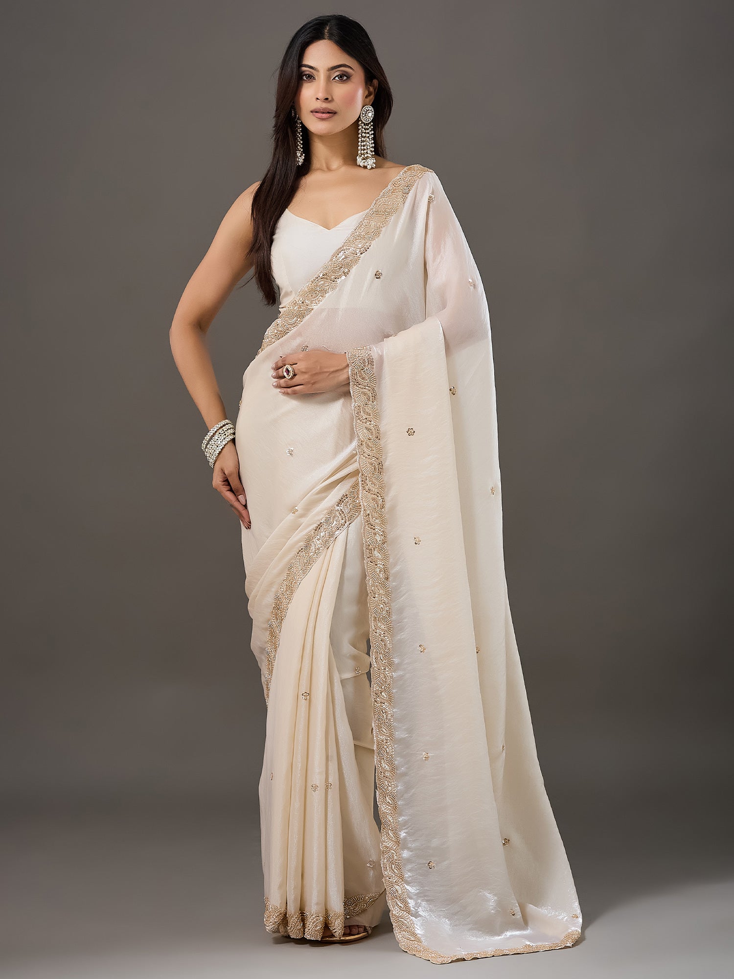Woman wearing cream satin saree with ornamented surface design and cream blouse