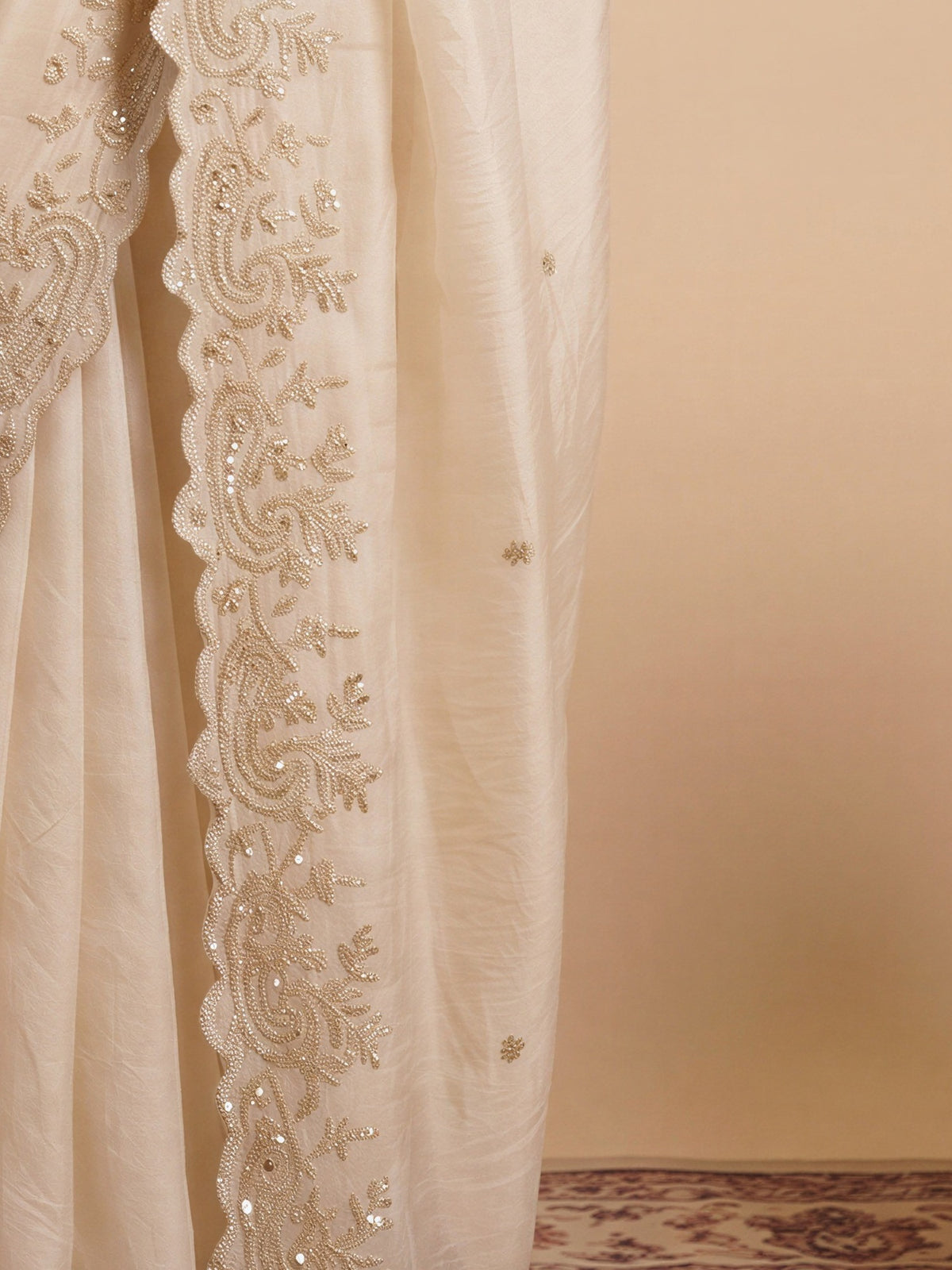 Pallu detail of off white satin saree showing ornamented surface design and embellished border