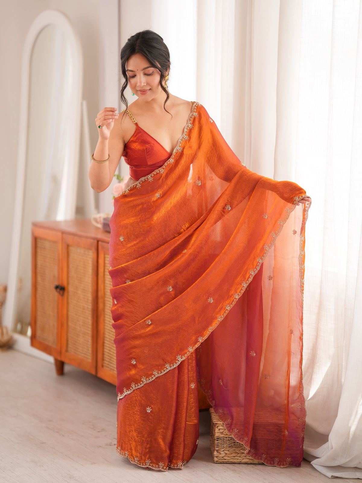 Woman wearing orange satin saree with ornamented surface design and orange blouse