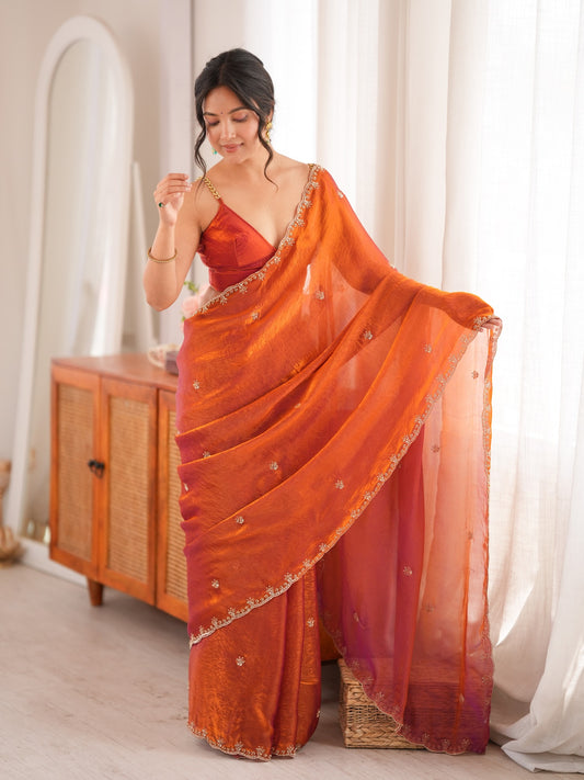 Woman wearing orange satin saree with ornamented surface design and orange blouse
