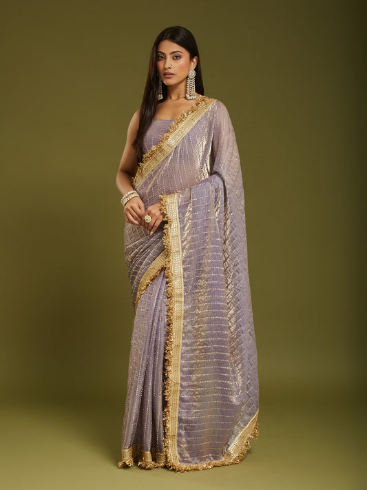 Woman wearing lavender satin saree with ornamented surface design and lavender blouse