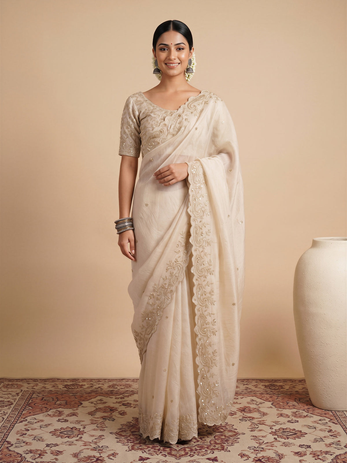 Woman wearing off white satin saree with ornamented surface design and off white blouse