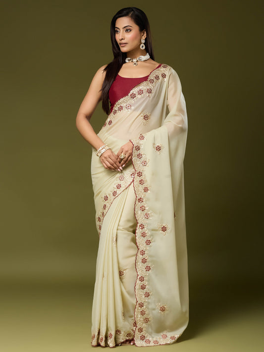 Woman wearing cream georgette saree with embroidered motif work and maroon blouse