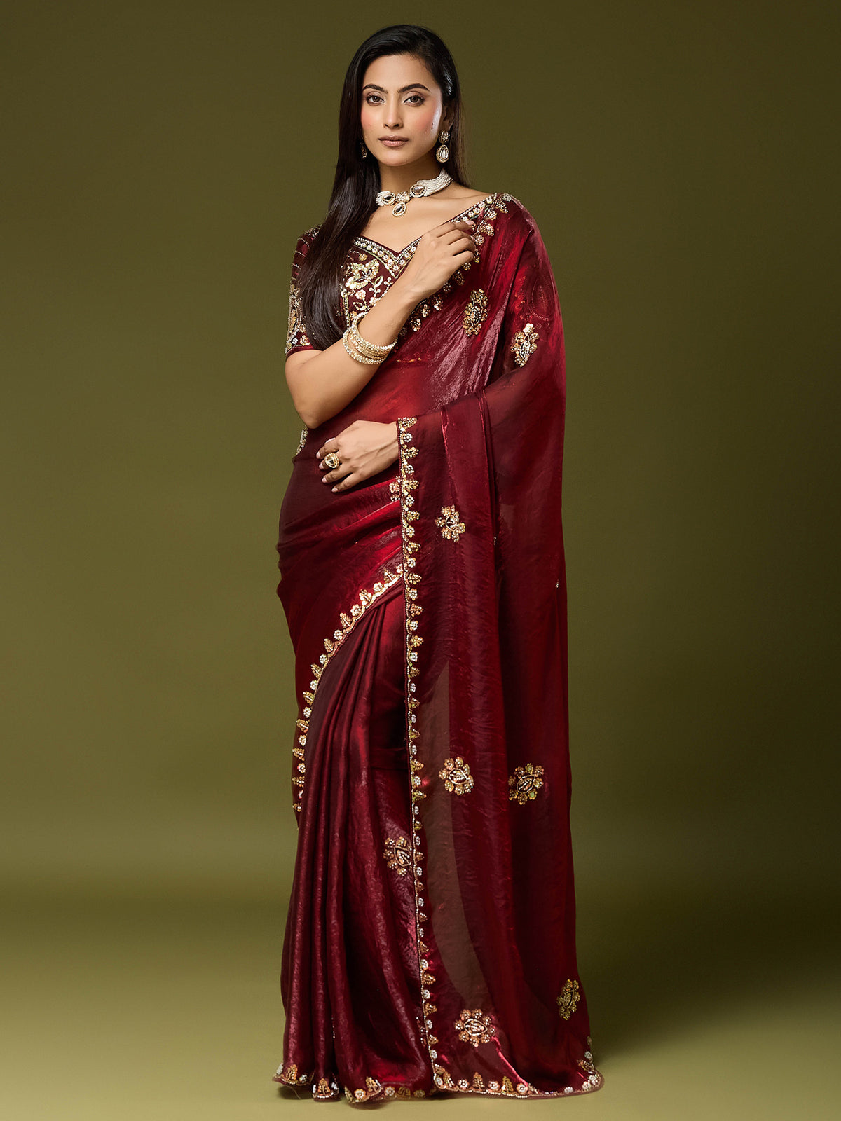 Woman wearing maroon satin silk saree with ornamented surface design and maroon blouse
