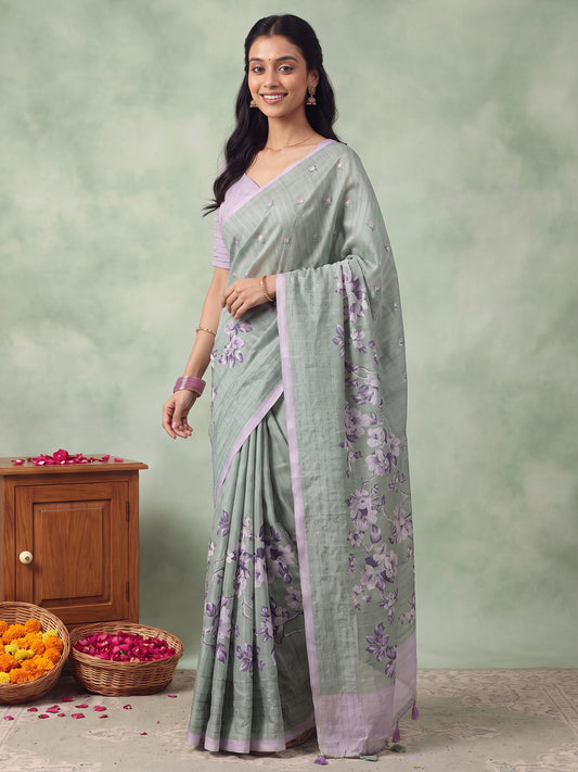 Woman wearing teal green silk blend saree with all-over floral design and lavender blouse