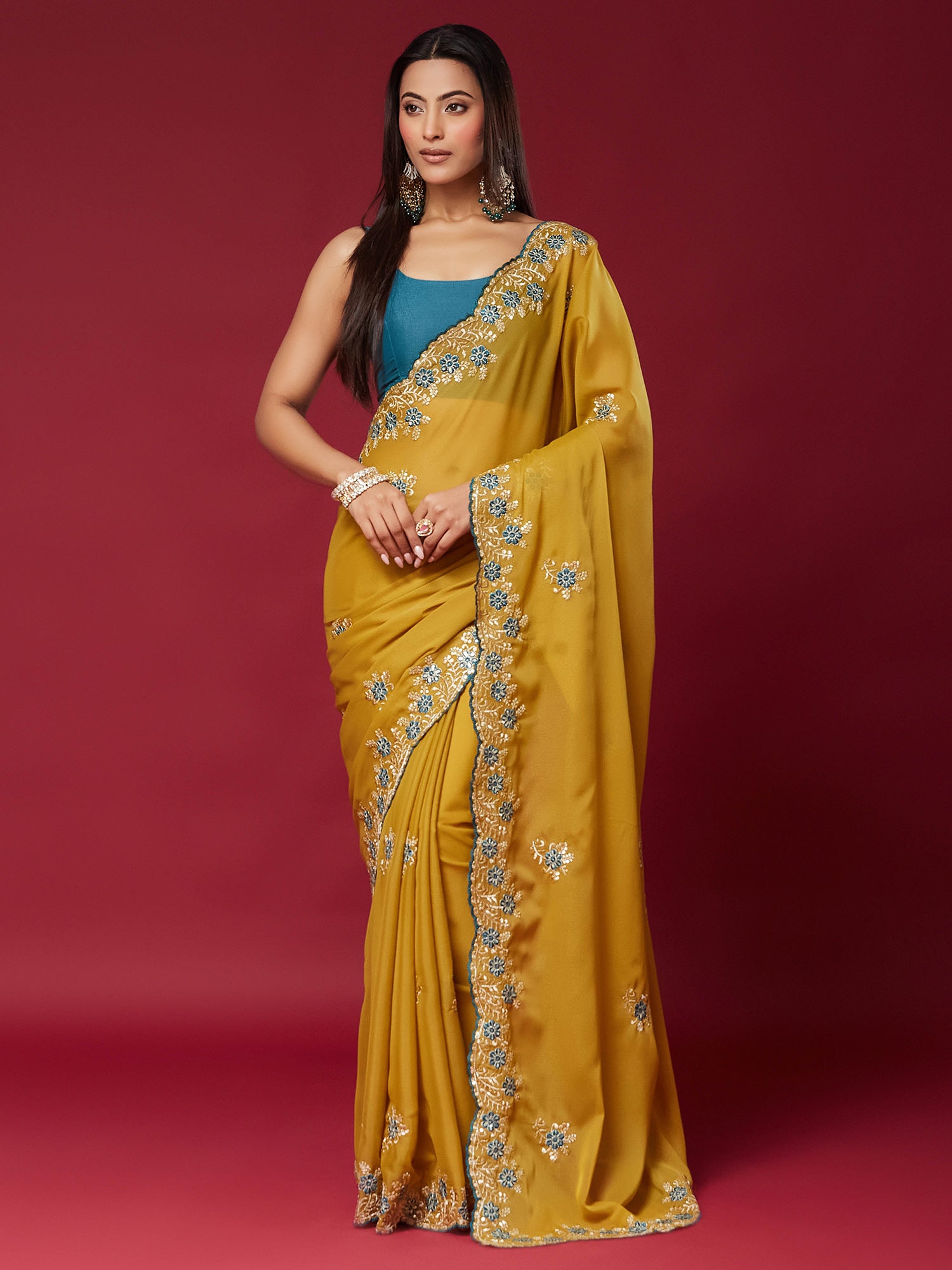 Woman wearing mustard georgette saree with embroidered motif work and teal blue blouse