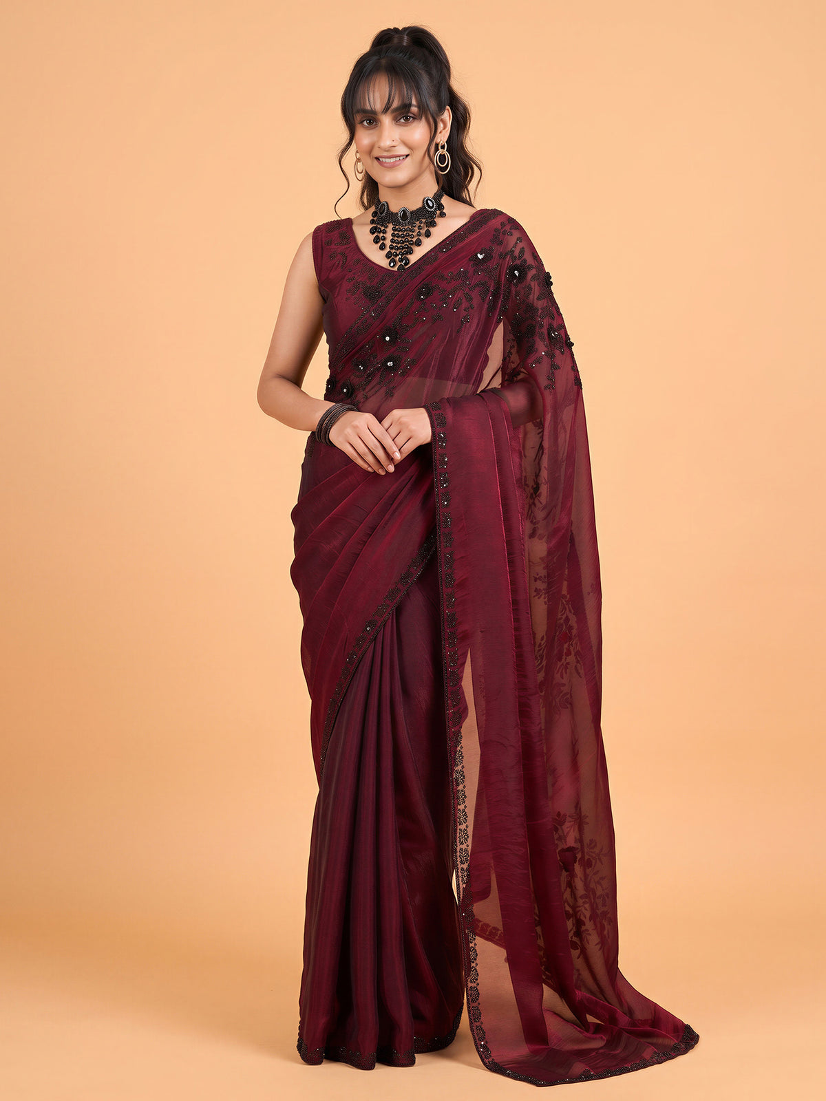 Woman wearing maroon satin silk saree with ornamented surface design and maroon blouse
