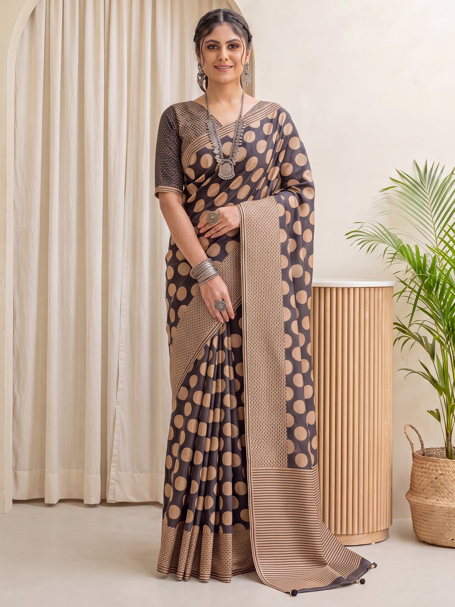 Woman wearing black silk blend saree with polka dot pattern and tan blouse