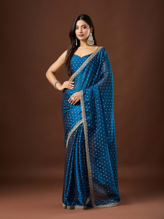 Woman wearing teal blue georgette saree with ornamented surface design and teal blue blouse
