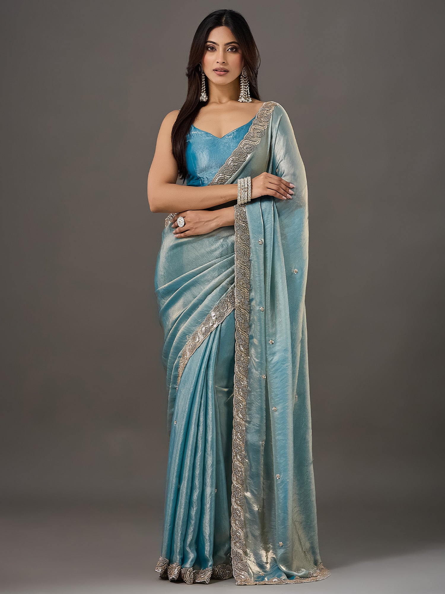 Woman wearing light blue satin saree with ornamented surface design and light blue blouse