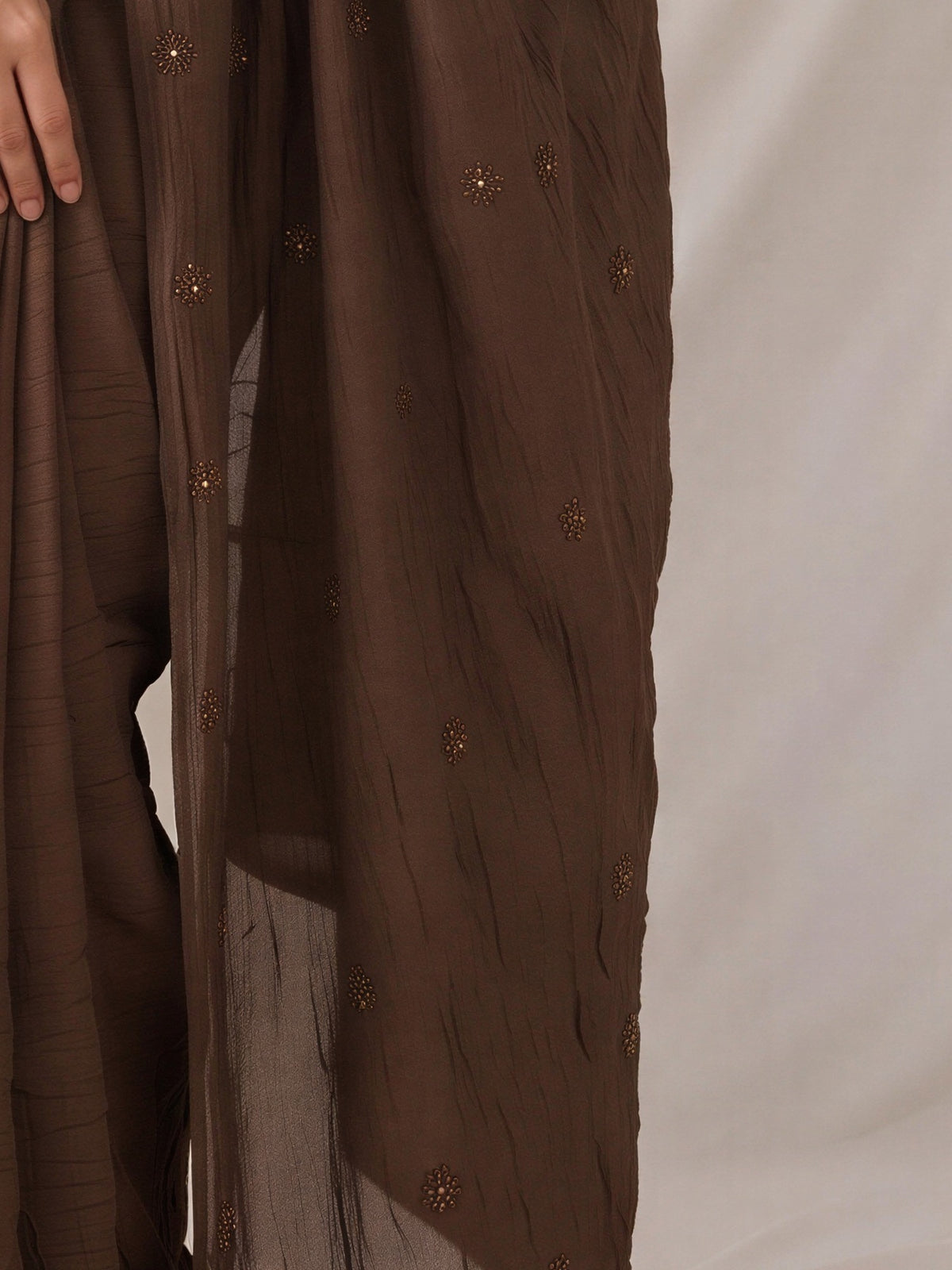 Pallu detail of brown poly crepe saree showing traditional indian motif work and solid border