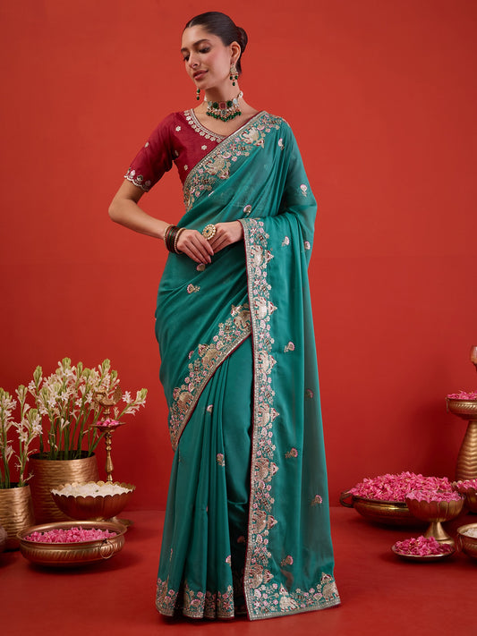 Woman wearing teal green georgette saree with ornamented surface design and maroon blouse