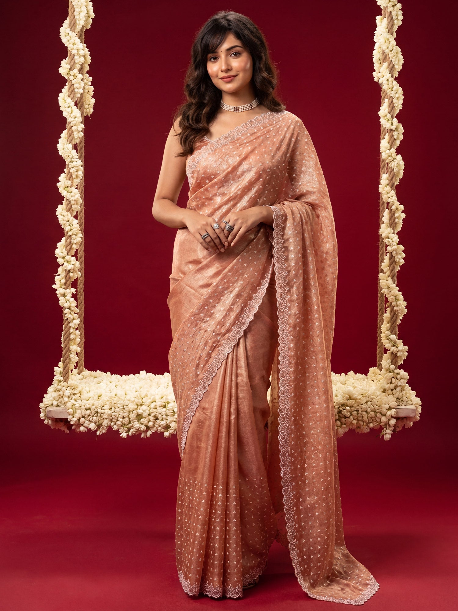 Woman wearing peach tissue saree with ornamented surface design and peach blouse