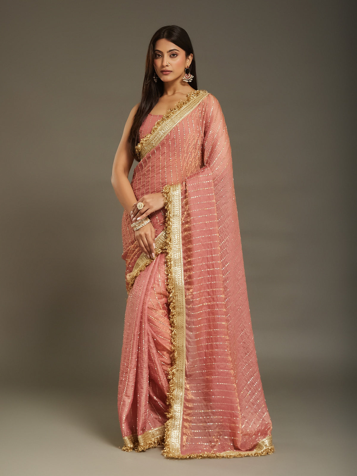 Woman wearing peach satin saree with ornamented surface design and peach blouse
