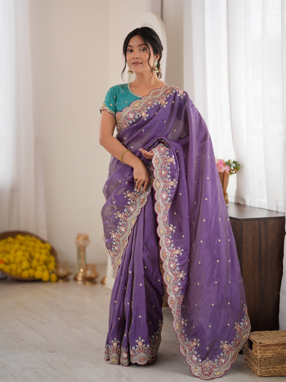 Woman wearing lavender satin saree with ornamented surface design and teal blue blouse