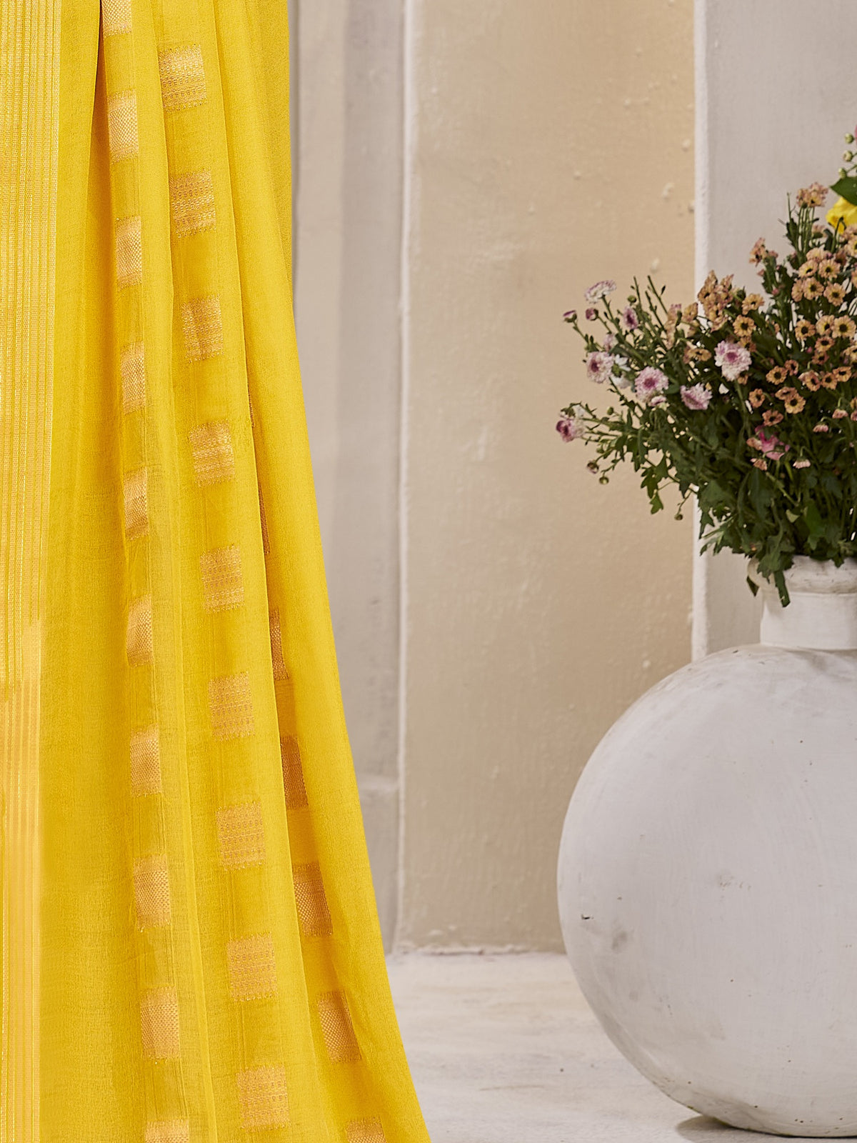 Pallu detail of yellow georgette saree showing zari butta (metallic motif) work and zari border