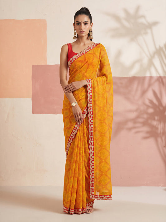 Woman wearing mustard georgette saree with bandhani tie-dye dot work and orange blouse
