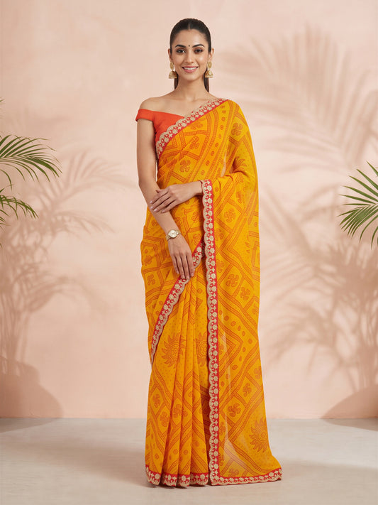 Woman wearing yellow georgette saree with bandhani tie-dye dot work and orange blouse