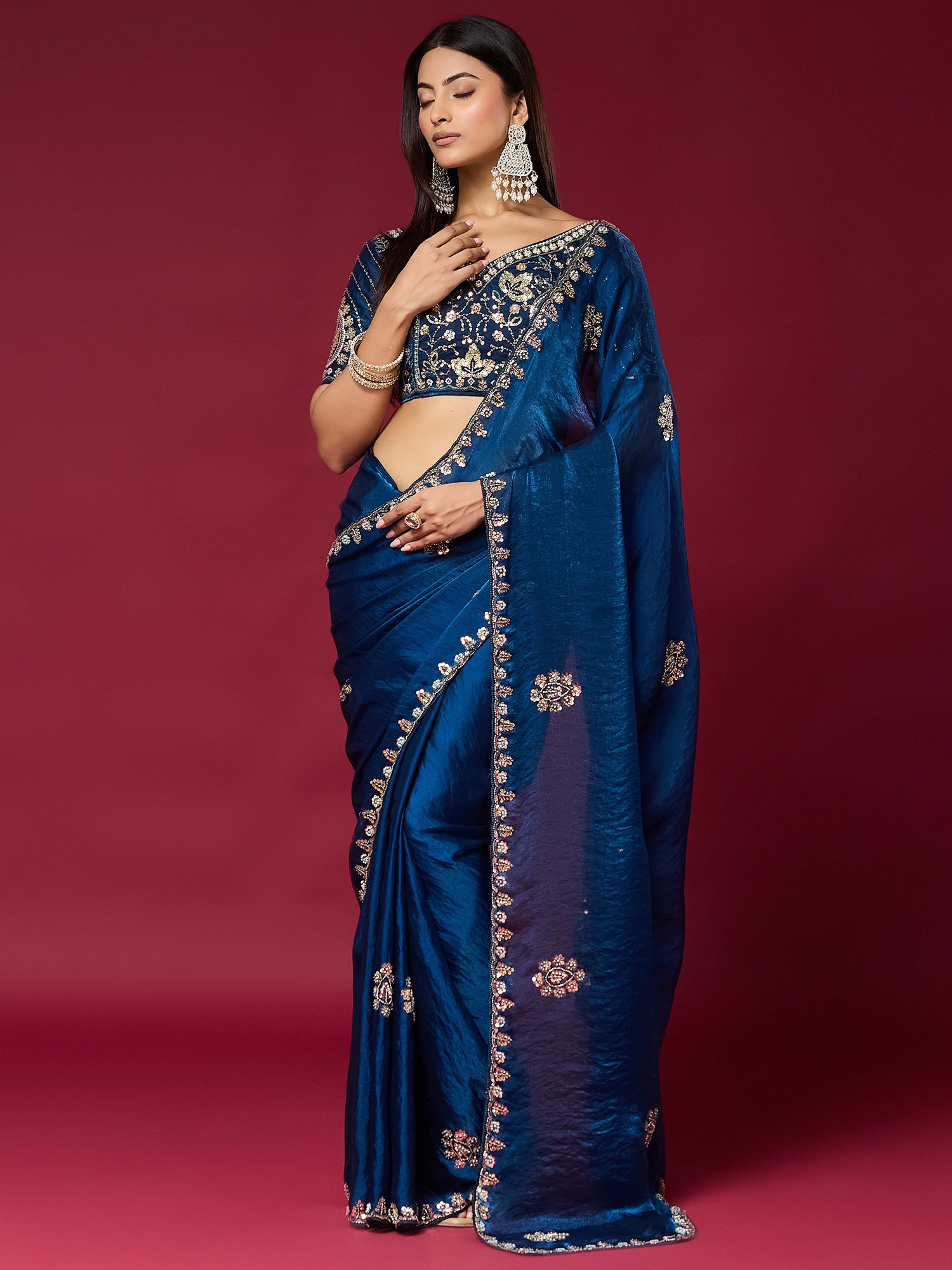 Woman wearing teal blue satin silk saree with ornamented surface design and teal blue blouse