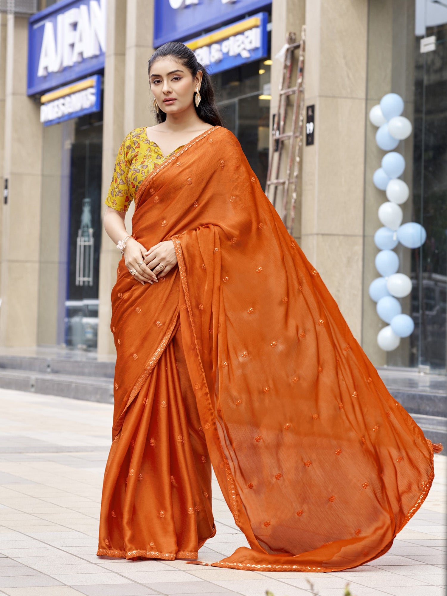 Woman wearing rust satin silk saree with ornamented surface design and mustard blouse