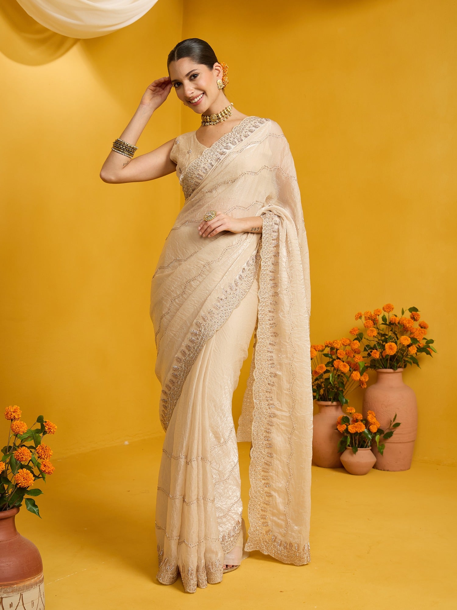 Woman wearing cream satin silk saree with ornamented surface design and cream blouse