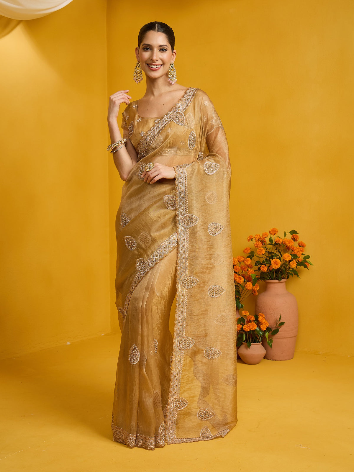 Woman wearing gold organza saree with ornamented surface design and gold blouse