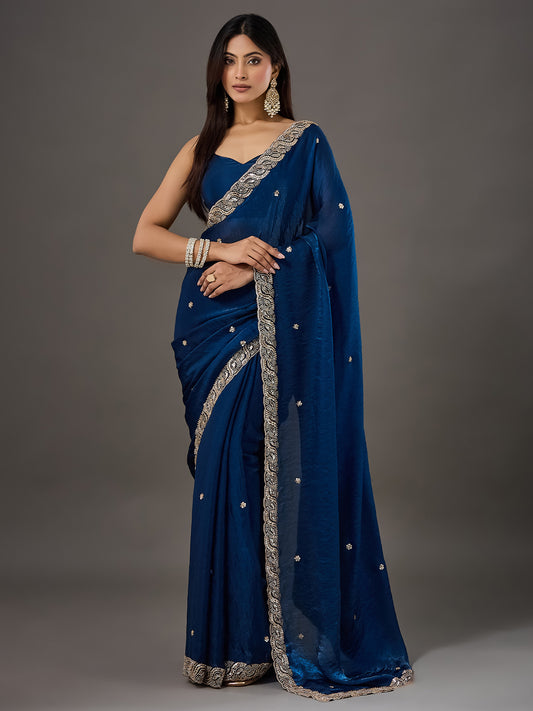 Woman wearing teal blue satin saree with ornamented surface design and teal blue blouse