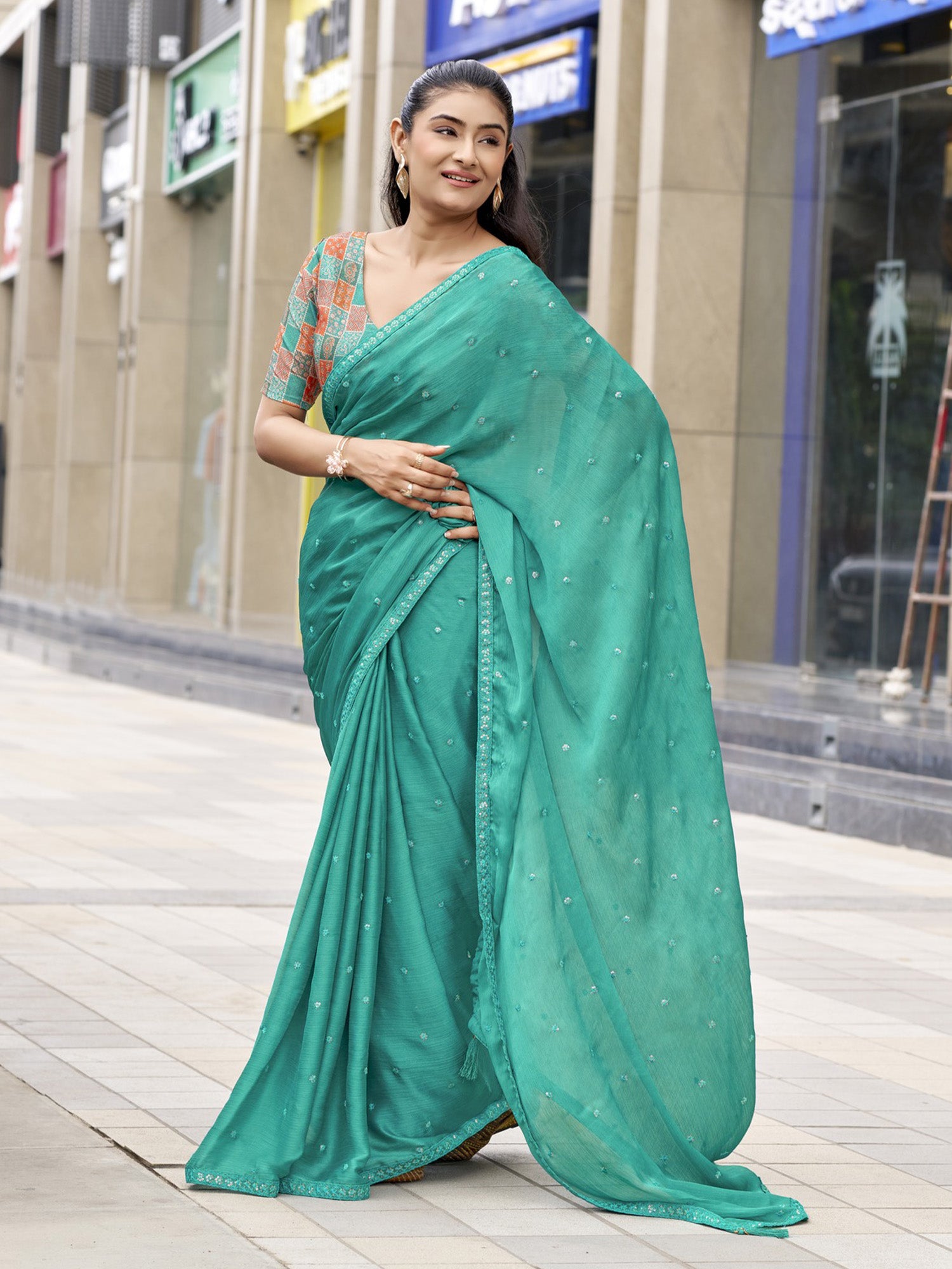 Woman wearing teal green satin silk saree with ornamented surface design and teal green blouse