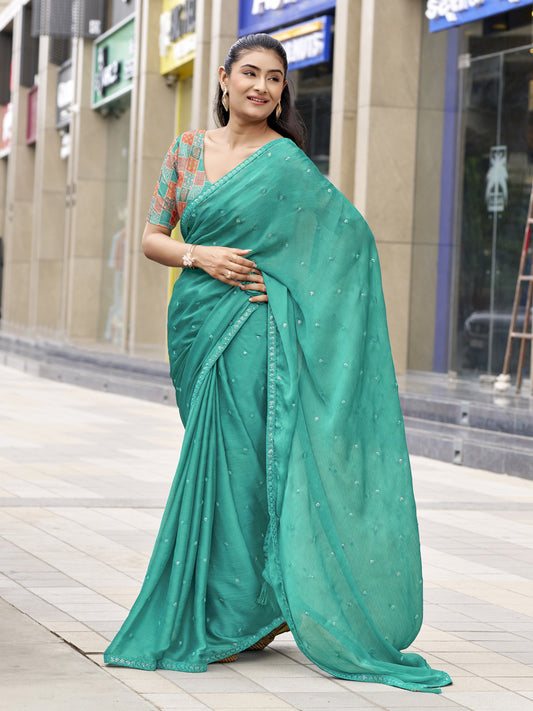 Woman wearing teal green satin silk saree with ornamented surface design and teal green blouse