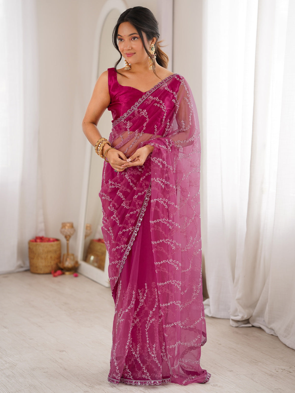 Woman wearing magenta net saree with ornamented surface design and magenta blouse