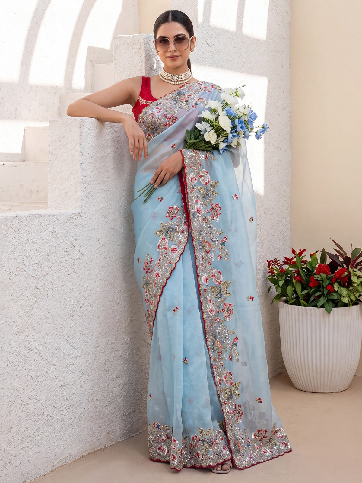 Woman wearing light blue organza saree with embroidered motif work and red blouse