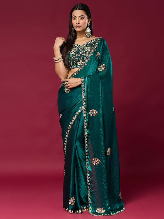 Woman wearing teal green satin silk saree with ornamented surface design and teal green blouse