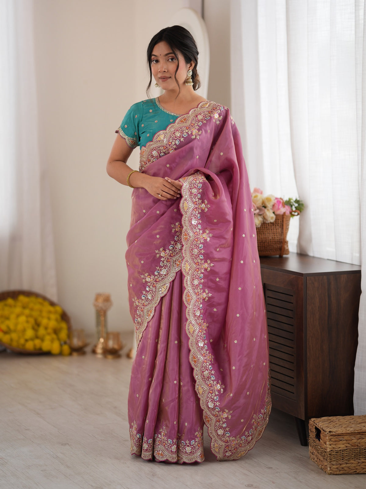 Woman wearing mauve satin saree with ornamented surface design and teal blue blouse