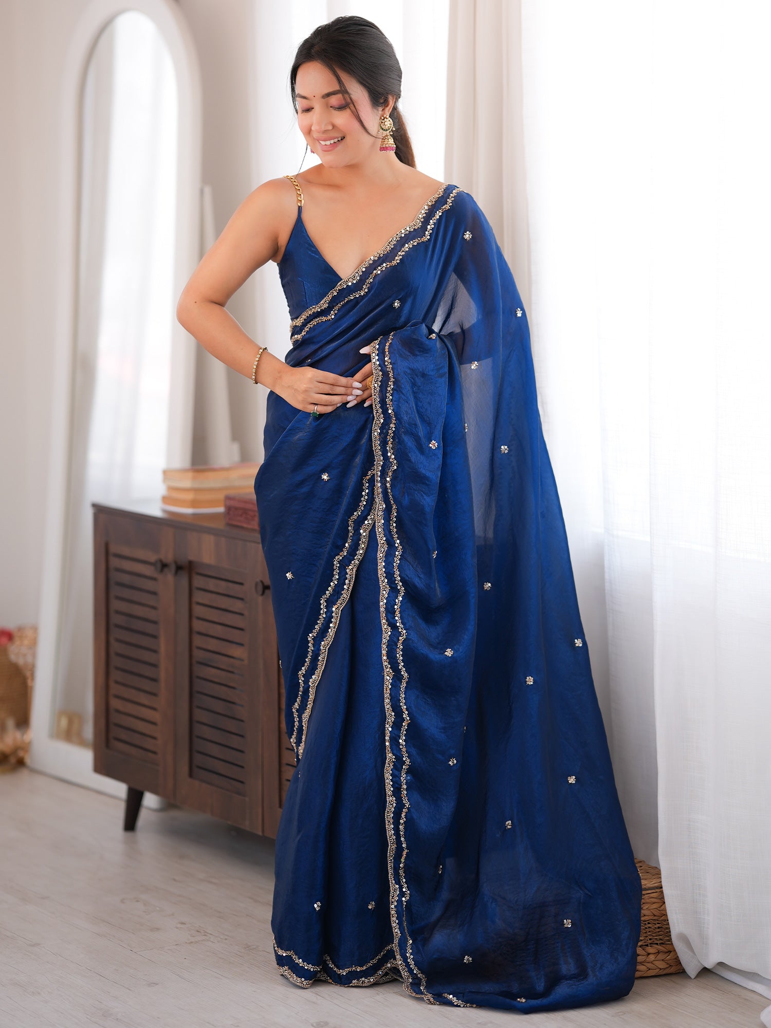 Woman wearing teal blue satin silk saree with ornamented surface design and teal blue blouse