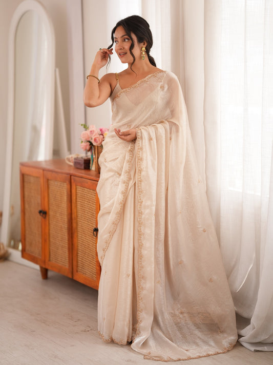 Woman wearing off white satin saree with ornamented surface design and off white blouse