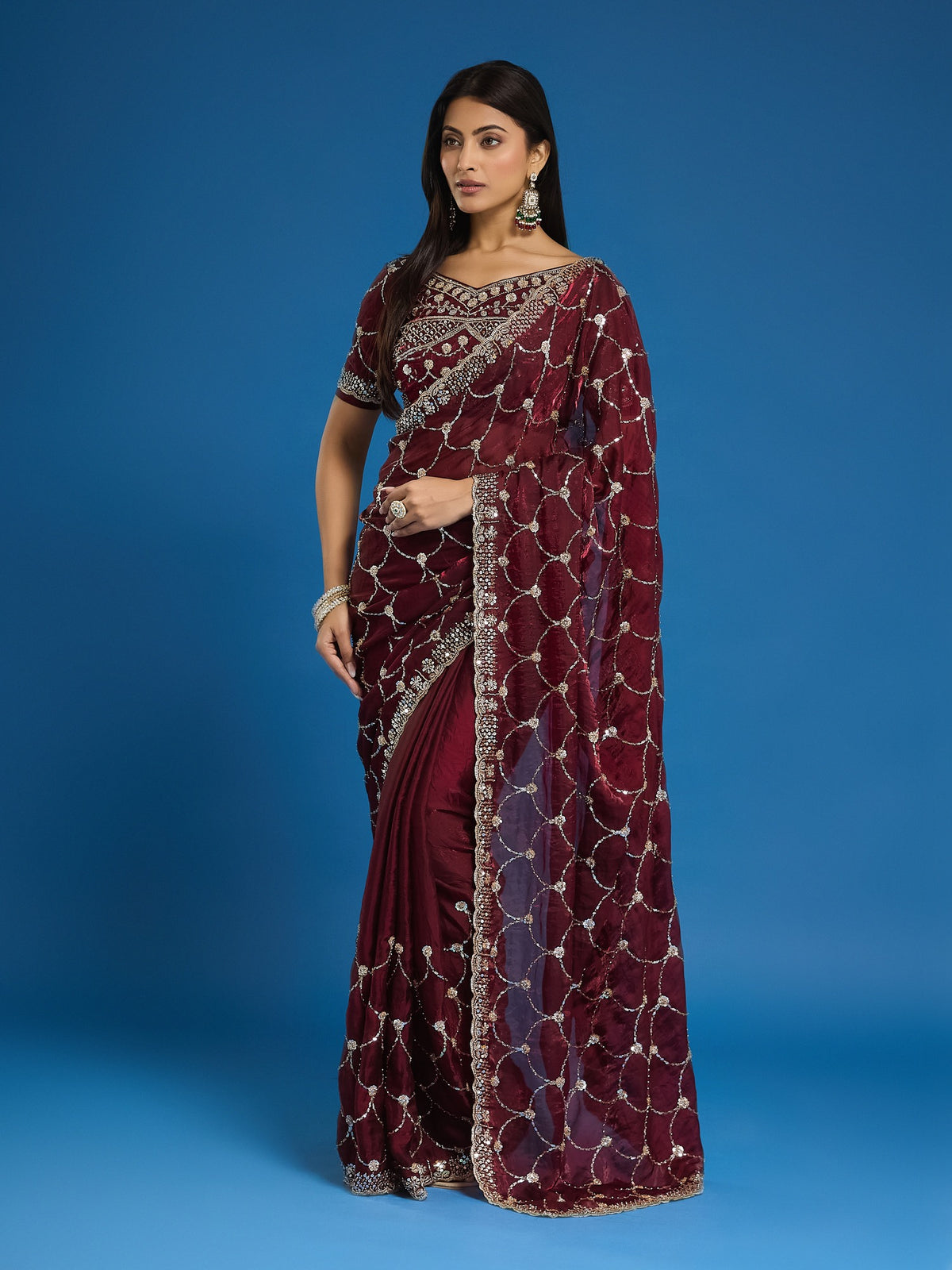 Woman wearing maroon satin saree with ornamented surface design and maroon blouse