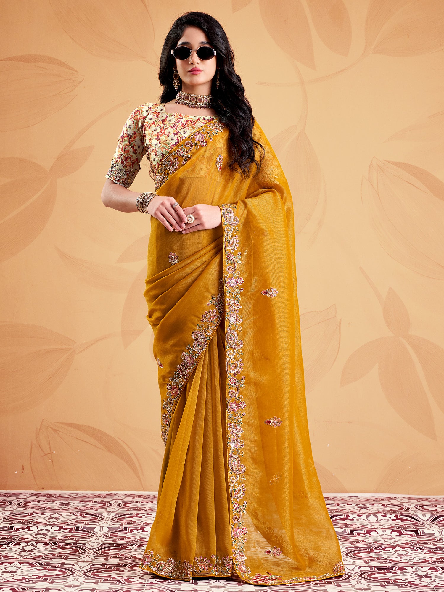 Woman wearing mustard tissue saree with ornamented surface design and multicolored blouse