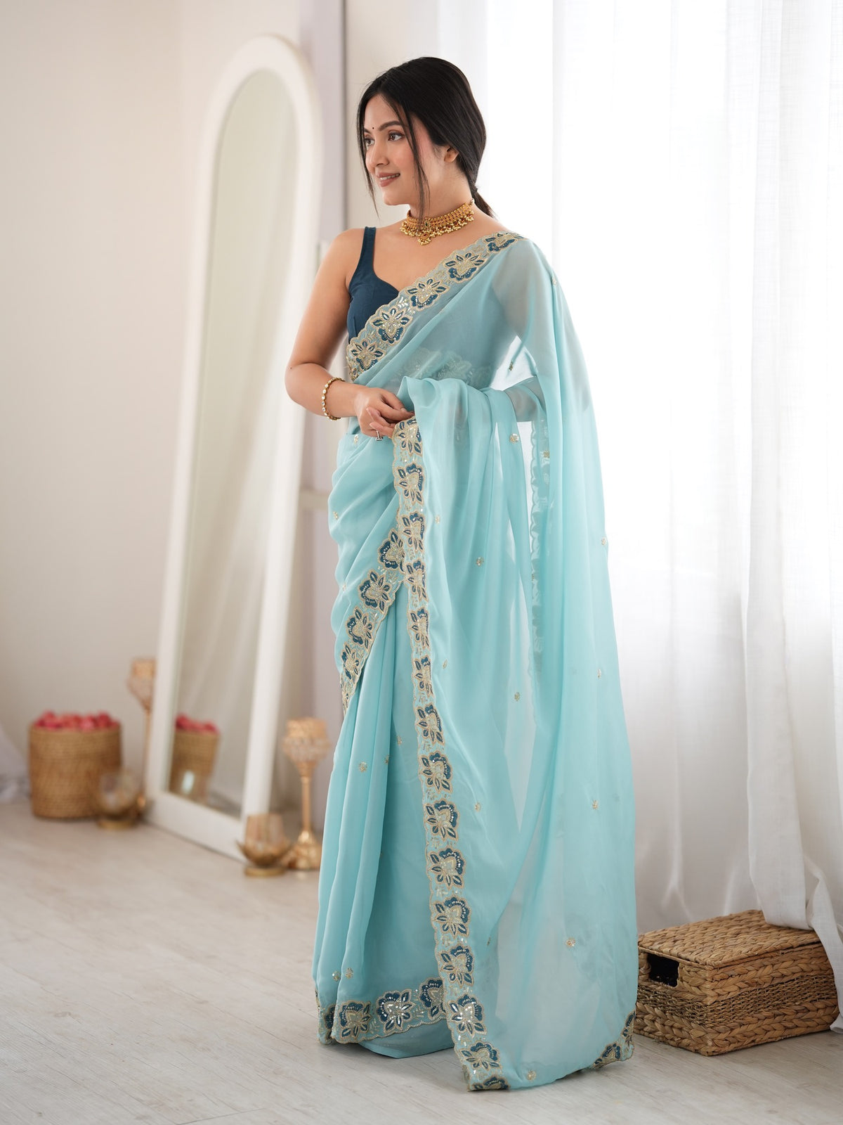 Woman wearing light blue georgette saree with ornamented surface design and teal blue blouse