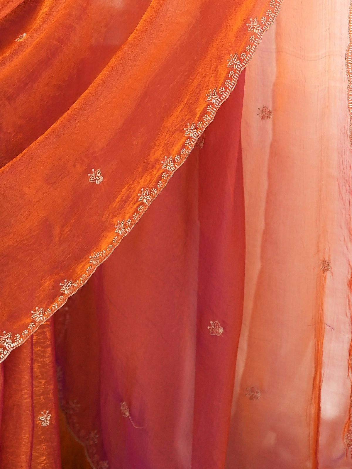 Pallu detail of orange satin saree showing ornamented surface design and embellished border